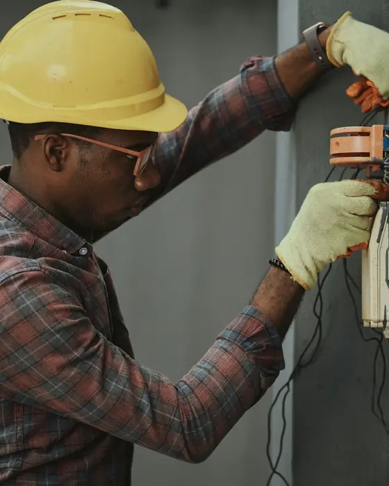 Técnico de capacete amarelo e luvas trabalhando em um painel elétrico