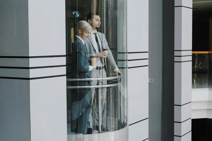 Mulher e homem conversando dentro de uma cabina de elevador de vidro