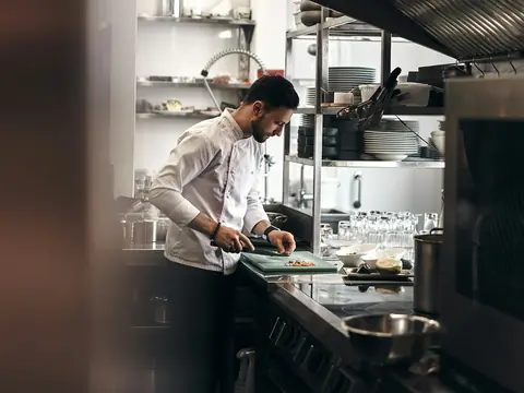 Cozinheiro de dólmã branco cortando legumes na cozinha de um restaurante